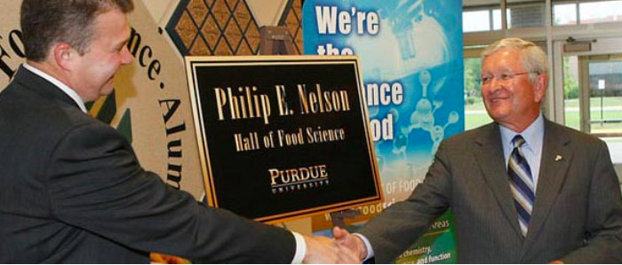 two men shake hands in front of a nelson plaque