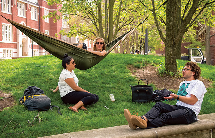 student relax near the union. one is in a hammock suspended from two trees